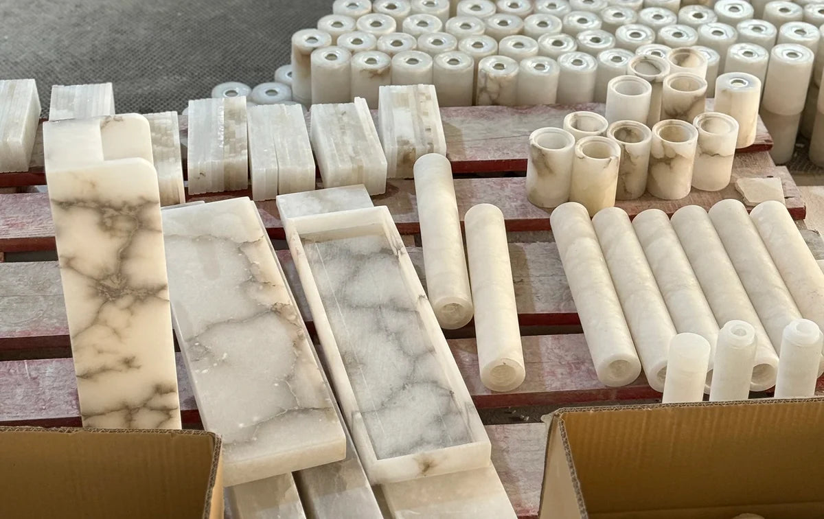 Shaped alabaster panels and cylindrical components prepared on a workshop bench.