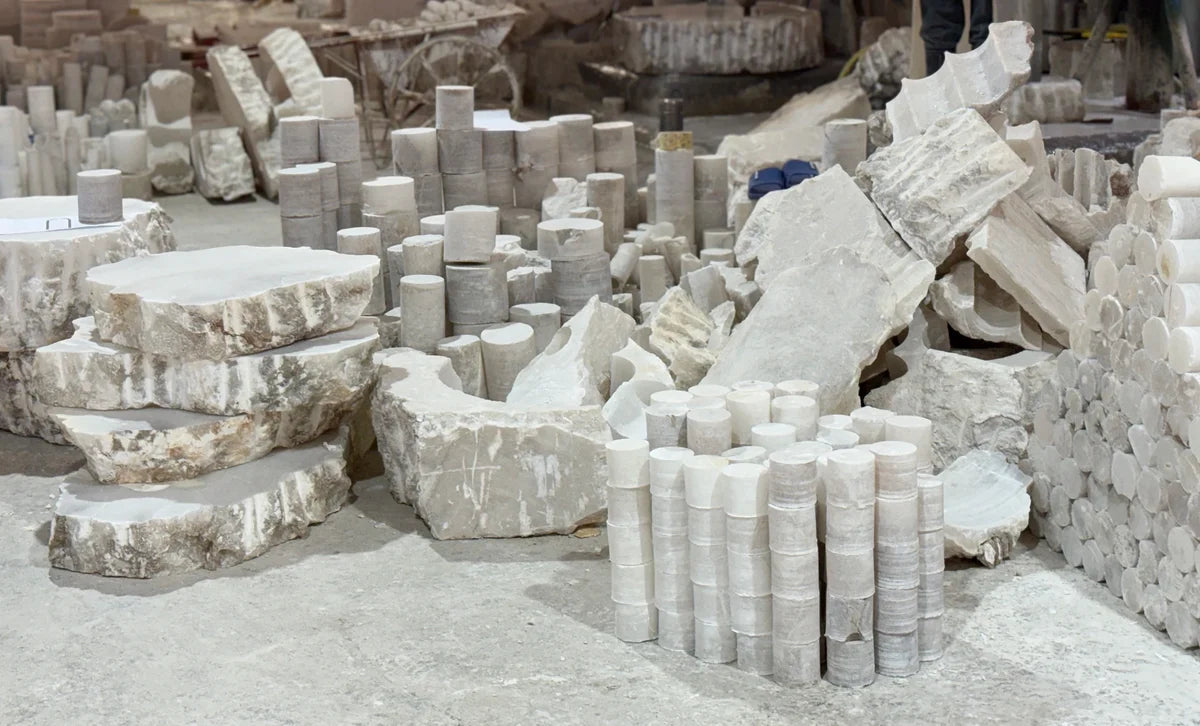 Alabaster slabs and cylindrical blanks arranged in a stone workshop.